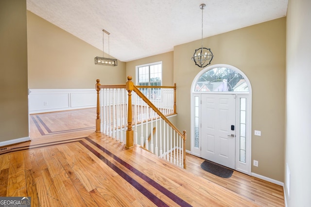 foyer entrance featuring lofted ceiling, a textured ceiling, a chandelier, and wood finished floors