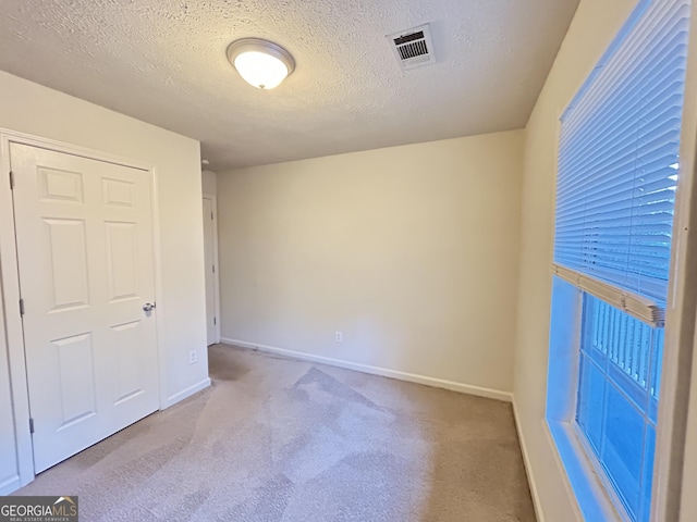 unfurnished room with carpet floors, visible vents, a textured ceiling, and baseboards
