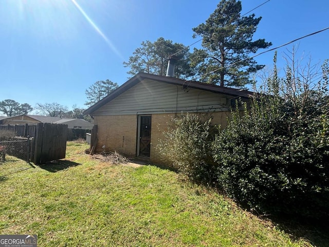 view of side of property with fence, a lawn, and brick siding