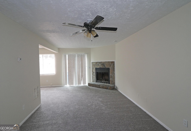 unfurnished living room with carpet, visible vents, ceiling fan, a stone fireplace, and a textured ceiling