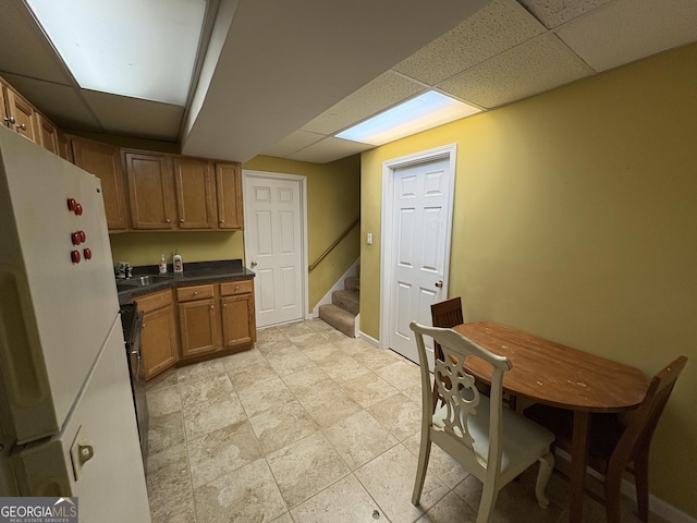 kitchen with brown cabinets, dark countertops, freestanding refrigerator, a drop ceiling, and baseboards