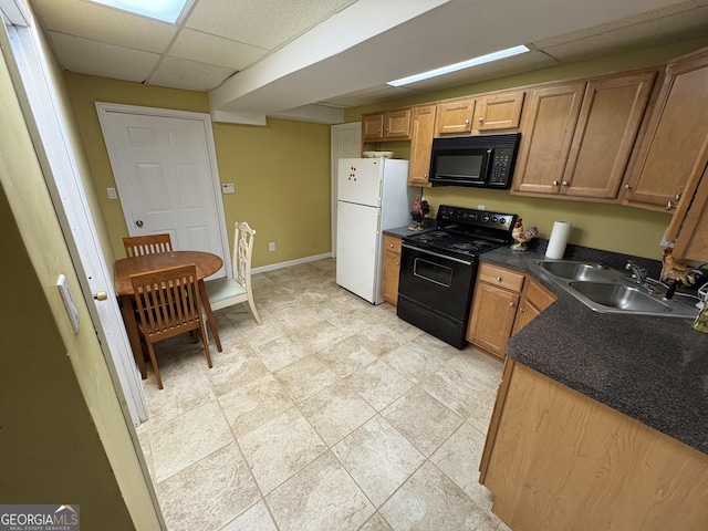 kitchen with a drop ceiling, a sink, baseboards, black appliances, and dark countertops