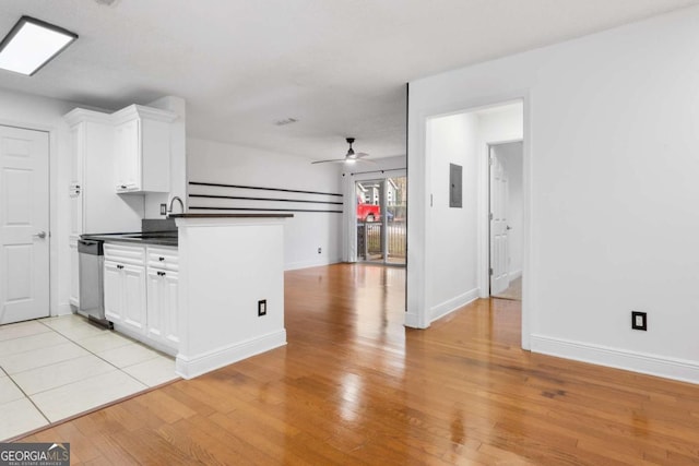 kitchen with light wood finished floors, dark countertops, ceiling fan, white cabinetry, and stainless steel dishwasher