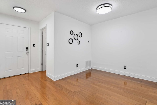 foyer with light wood-type flooring, visible vents, a textured ceiling, and baseboards