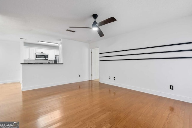 unfurnished living room featuring ceiling fan, visible vents, baseboards, and wood finished floors