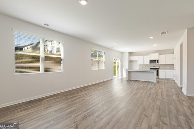 unfurnished living room with light wood-type flooring, baseboards, and recessed lighting