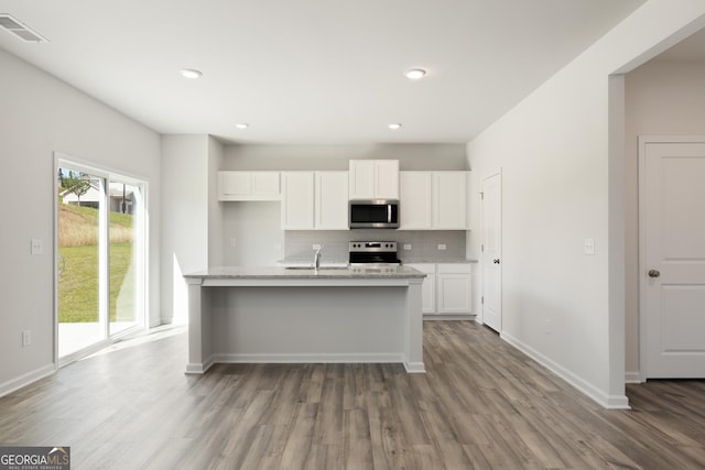 kitchen featuring stainless steel appliances, wood finished floors, backsplash, white cabinetry, and light stone counters