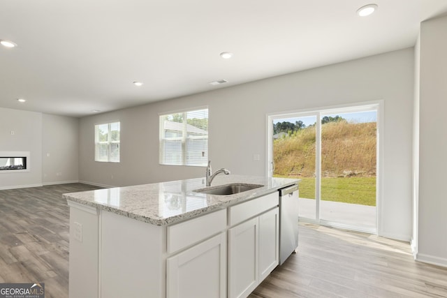 kitchen with a sink, stainless steel dishwasher, light wood-type flooring, a glass covered fireplace, and recessed lighting