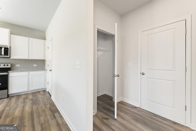 kitchen featuring stainless steel appliances, light wood-type flooring, tasteful backsplash, and white cabinets