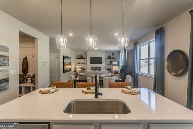 kitchen with an island with sink, light stone counters, a sink, and hanging light fixtures