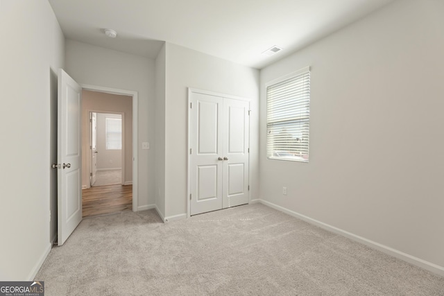 unfurnished bedroom with light colored carpet, multiple windows, baseboards, and a closet