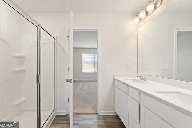 full bathroom featuring wood finished floors, a stall shower, double vanity, and baseboards