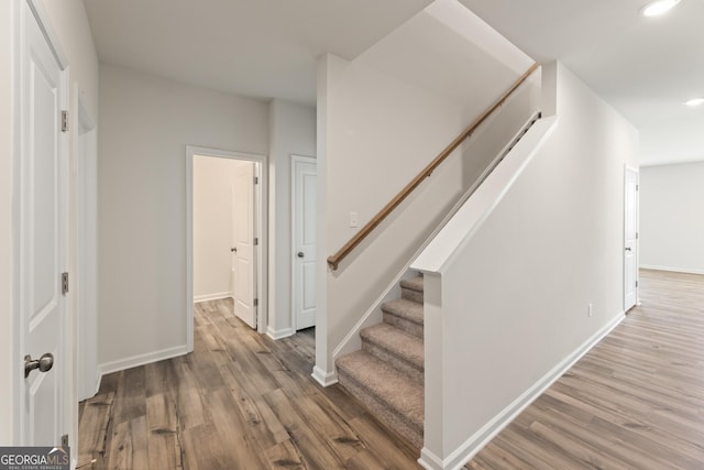 staircase with wood finished floors, baseboards, and recessed lighting