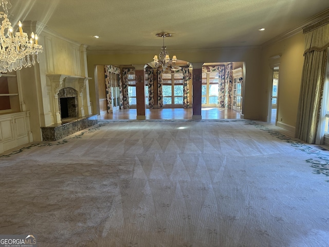 unfurnished dining area featuring decorative columns, a premium fireplace, ornamental molding, carpet flooring, and a chandelier