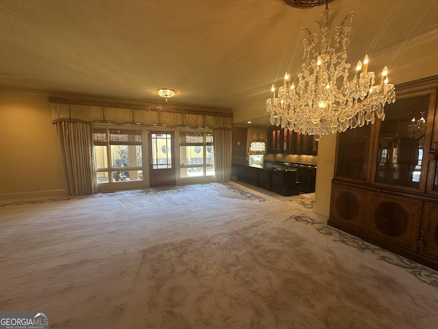 unfurnished living room with baseboards, ornamental molding, carpet, a textured ceiling, and a notable chandelier