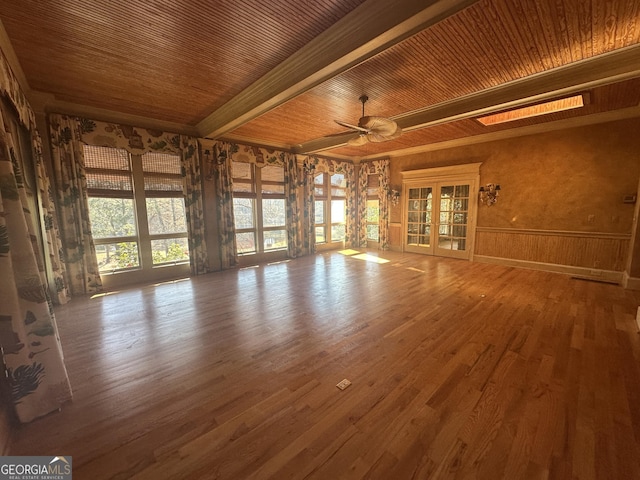 unfurnished living room with a healthy amount of sunlight, french doors, beam ceiling, and wood finished floors