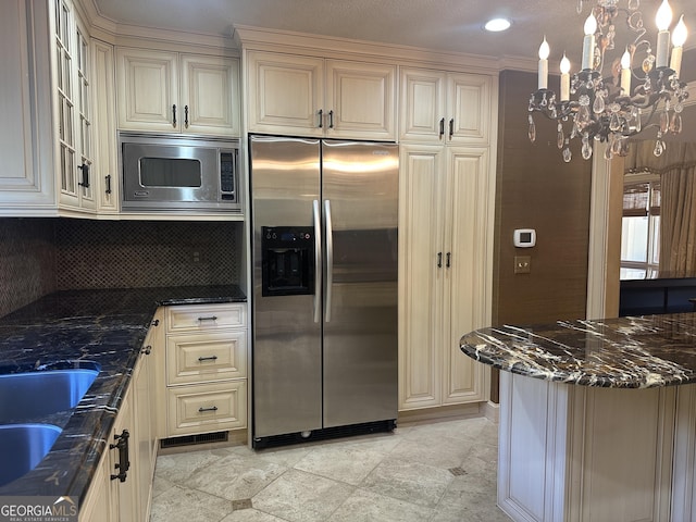 kitchen featuring stainless steel appliances, decorative backsplash, cream cabinets, glass insert cabinets, and dark stone counters