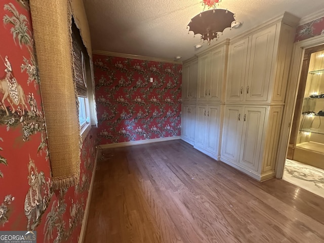 unfurnished bedroom with light wood-style flooring, ornamental molding, a textured ceiling, baseboards, and wallpapered walls