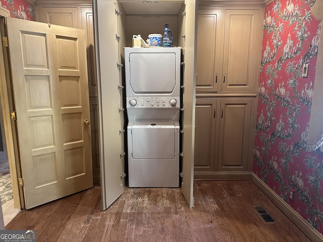 washroom featuring dark wood-style flooring, stacked washer / drying machine, visible vents, laundry area, and wallpapered walls