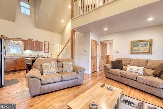 living room featuring stairway, light wood-type flooring, a towering ceiling, and recessed lighting