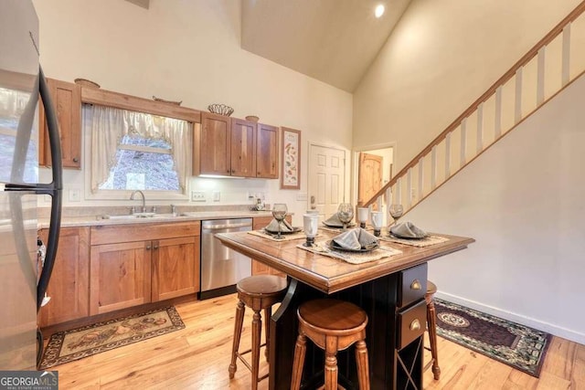 kitchen featuring stainless steel appliances, high vaulted ceiling, a sink, and light wood-style floors