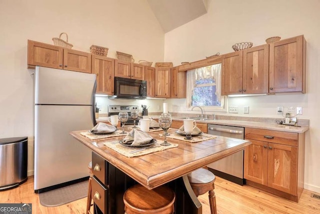 kitchen with light wood finished floors, stainless steel appliances, light countertops, a sink, and high vaulted ceiling