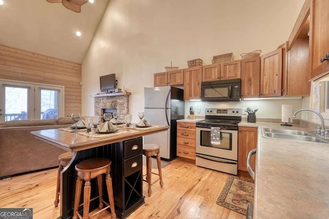 kitchen with high vaulted ceiling, light wood-style flooring, a sink, light countertops, and appliances with stainless steel finishes