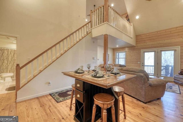 living area featuring light wood-style flooring, wood walls, a towering ceiling, baseboards, and stairs