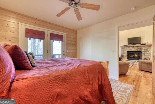 bedroom featuring light wood-style flooring, ceiling fan, access to exterior, a stone fireplace, and wood walls