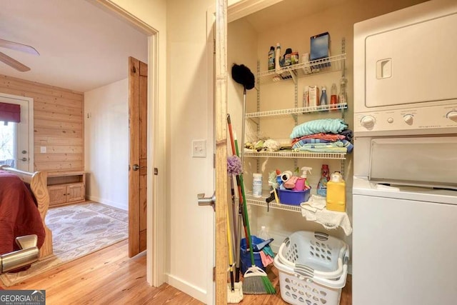 clothes washing area featuring stacked washer and dryer, ceiling fan, wood walls, wood finished floors, and laundry area