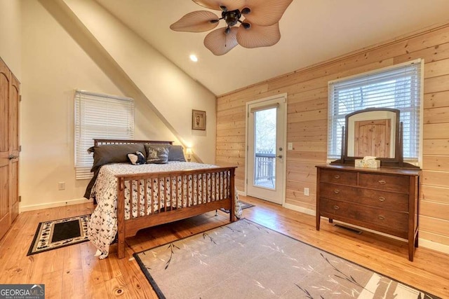 bedroom featuring vaulted ceiling, access to outside, wood-type flooring, and wooden walls