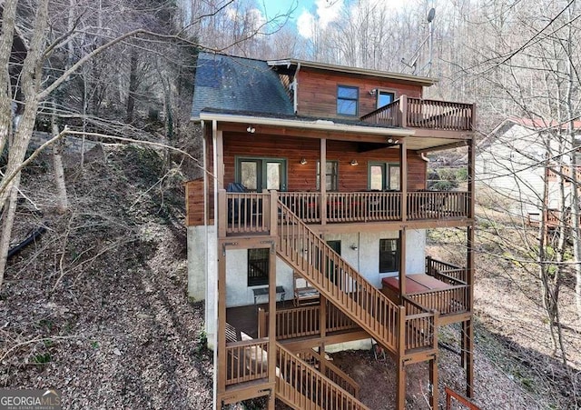 rear view of property featuring a shingled roof, stairway, and a deck