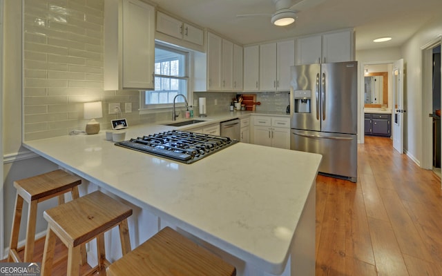 kitchen featuring stainless steel appliances, a peninsula, a sink, white cabinetry, and light countertops