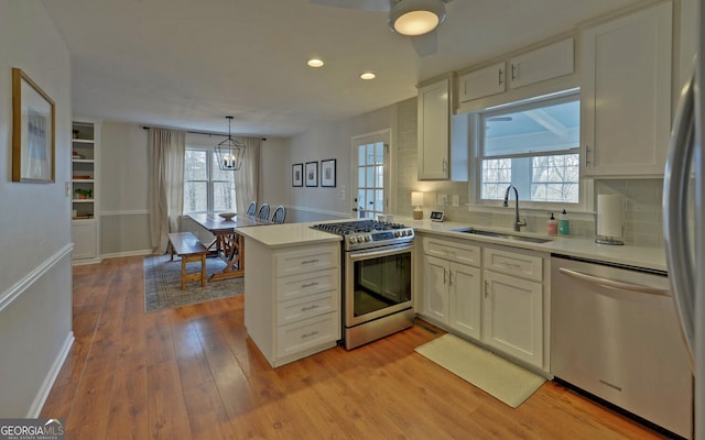 kitchen with appliances with stainless steel finishes, a peninsula, light countertops, white cabinetry, and a sink