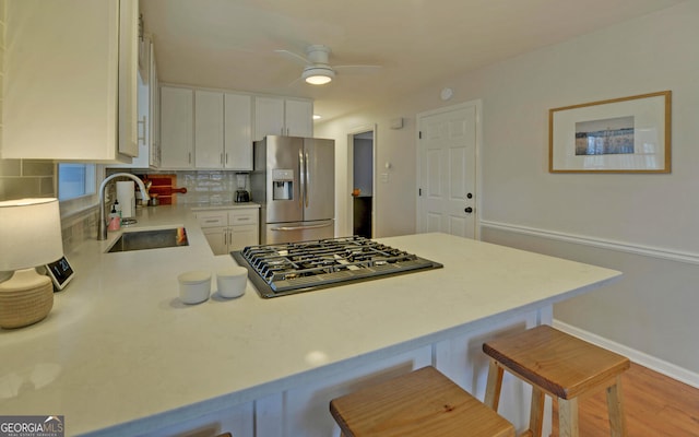 kitchen featuring stainless steel fridge with ice dispenser, a peninsula, gas stovetop, a kitchen bar, and a sink