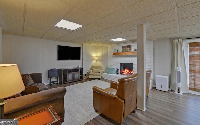 living room featuring a drop ceiling, a fireplace, and wood finished floors