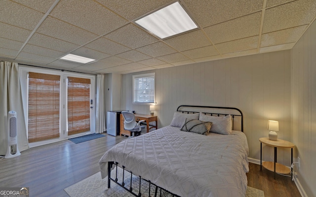 bedroom featuring access to exterior, a drop ceiling, and wood finished floors