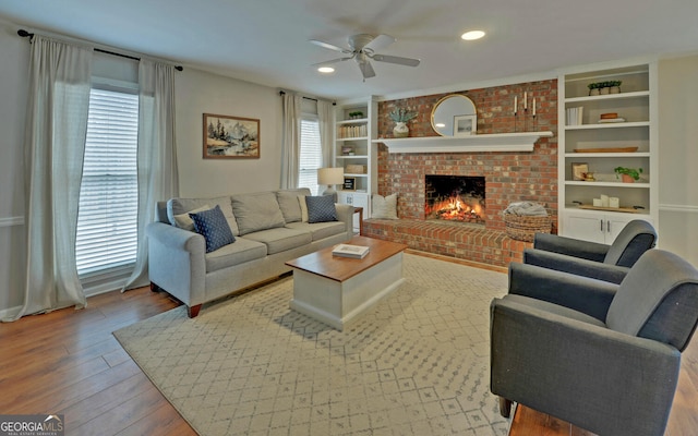 living area featuring built in features, recessed lighting, a ceiling fan, a brick fireplace, and wood finished floors