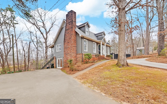 view of side of property featuring stairs, driveway, brick siding, and a chimney