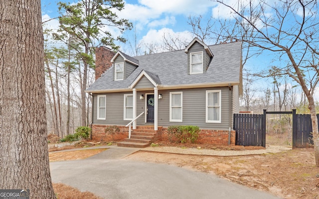 new england style home with a shingled roof, fence, and a chimney