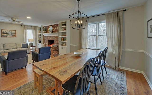 dining room with ceiling fan, a fireplace, wood finished floors, and baseboards