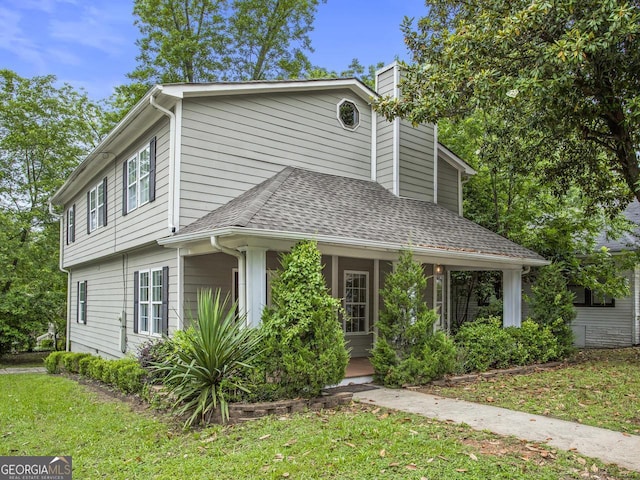 view of front of home with roof with shingles, a front lawn, and a chimney