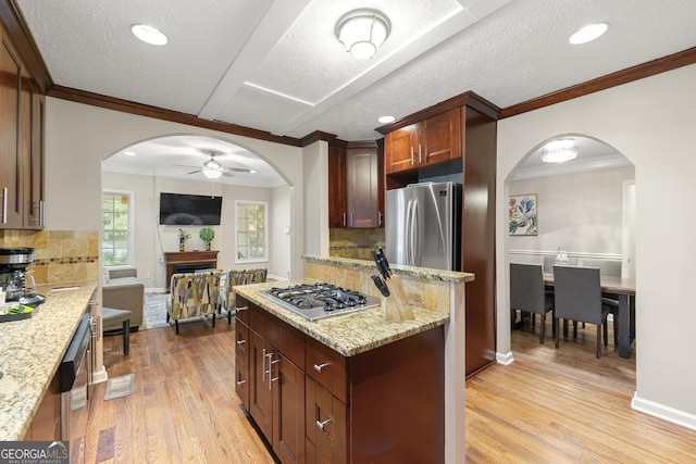 kitchen featuring arched walkways, a kitchen island, appliances with stainless steel finishes, light stone countertops, and light wood finished floors