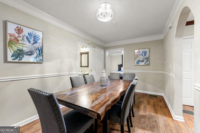 dining room with arched walkways, ornamental molding, a textured ceiling, wood finished floors, and baseboards