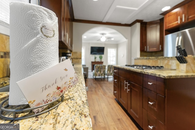 kitchen featuring arched walkways, light wood-style flooring, light stone countertops, crown molding, and stainless steel gas stovetop