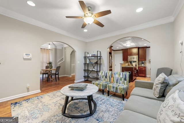 living room featuring ornamental molding, arched walkways, baseboards, and light wood finished floors