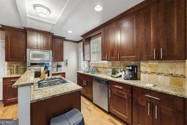 kitchen with tasteful backsplash, appliances with stainless steel finishes, light stone counters, light wood-style floors, and a sink