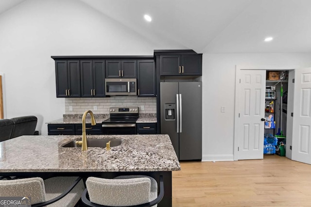 kitchen featuring light stone counters, light wood-style flooring, a sink, vaulted ceiling, and appliances with stainless steel finishes