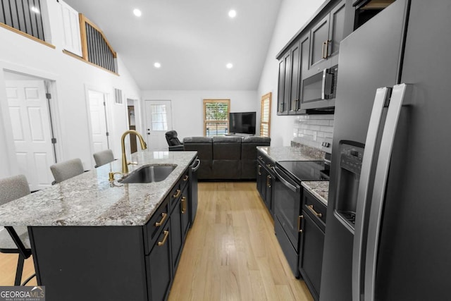 kitchen featuring a breakfast bar area, a sink, light wood-style floors, appliances with stainless steel finishes, and a center island with sink