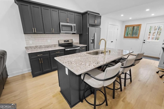 kitchen featuring tasteful backsplash, appliances with stainless steel finishes, a breakfast bar, light wood-type flooring, and a sink